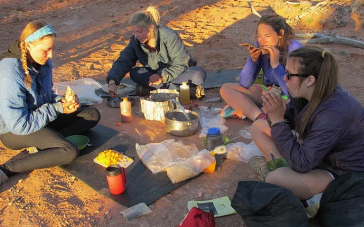 Four people sit on the ground while cooking and eating.
